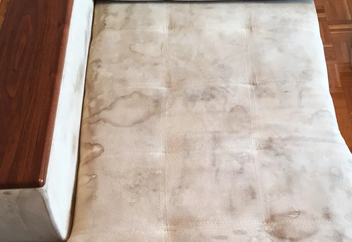 The same microfibre chaise before cleaning &mdash; heavy watermarks and soiling across the seat.